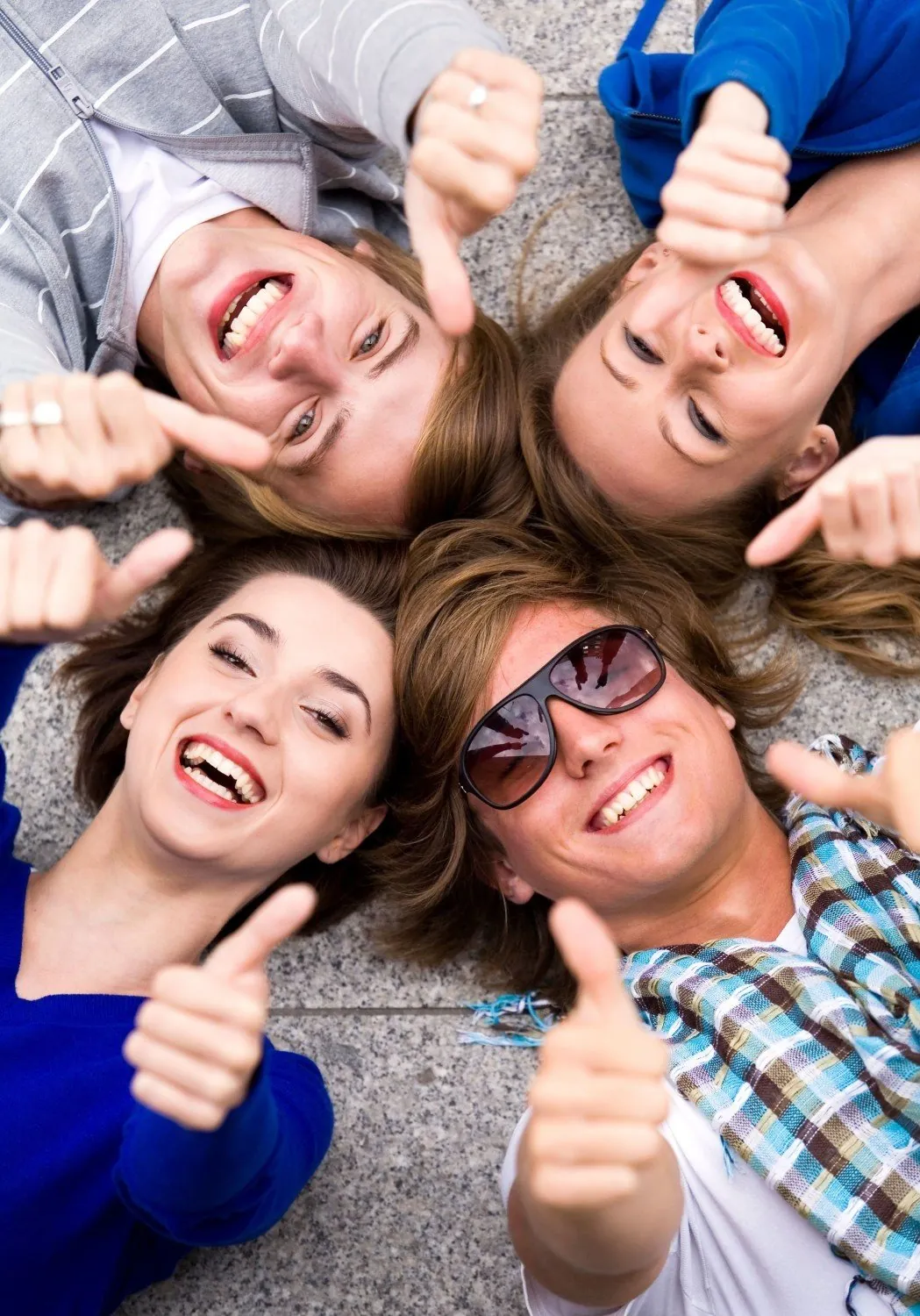 Four smiling students lying in a circle, giving a thumbs up